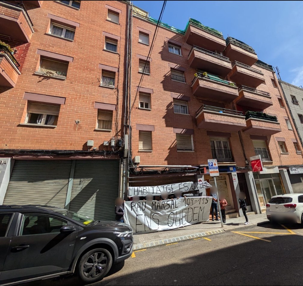 Fachada del edificio con pancartas: «L'habitatge és...» y «Pau Marsal 107-115 ens quedem»